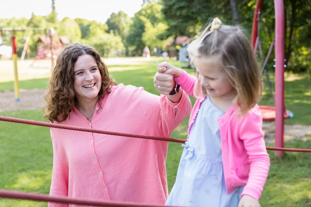 Coachin lacht gemeinsam mit einem Mädchen an einem Klettergerüst auf dem Spielplatz
