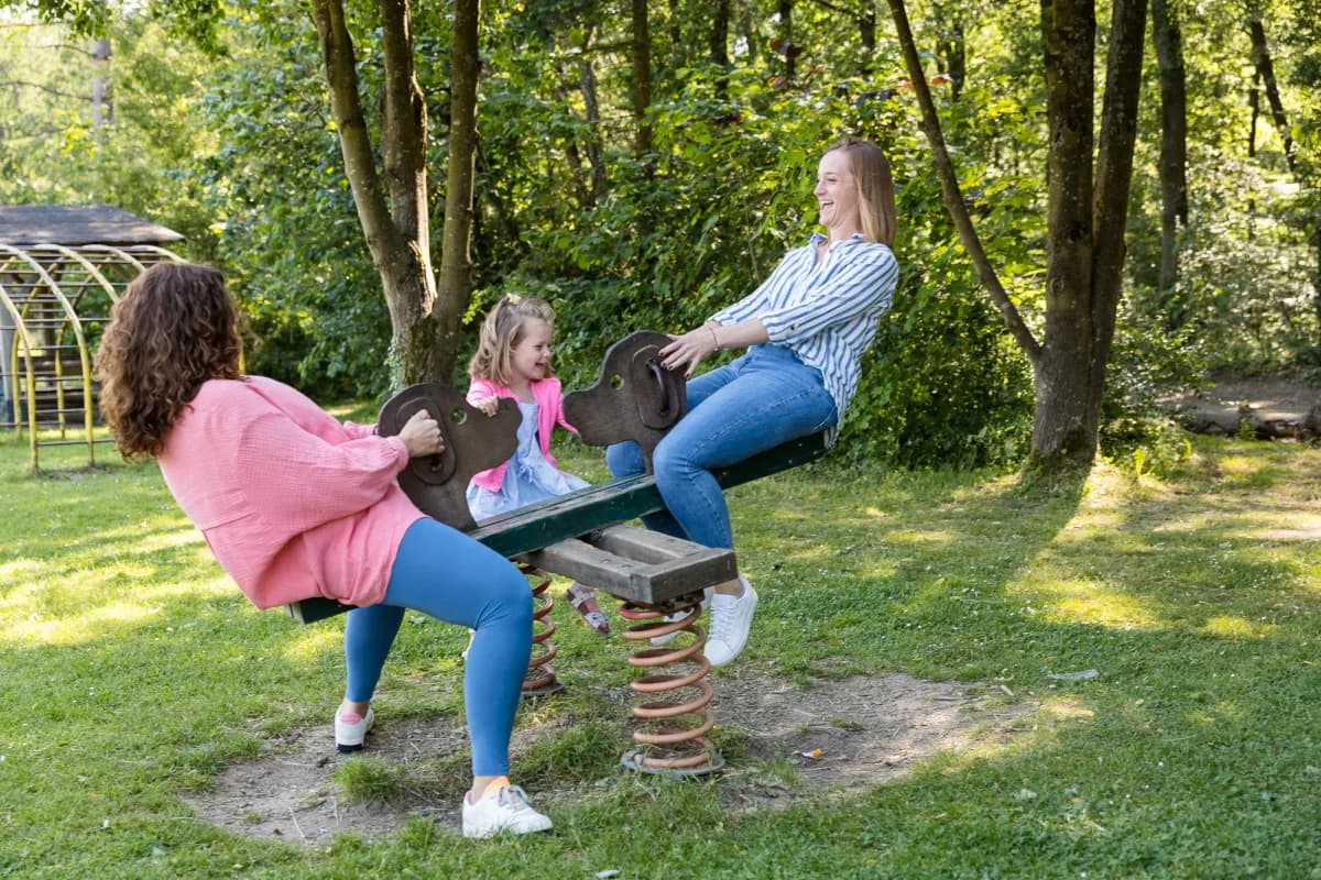 Zwei Frauen und ein Kind balancieren gemeinsam auf einer Wippe im Park