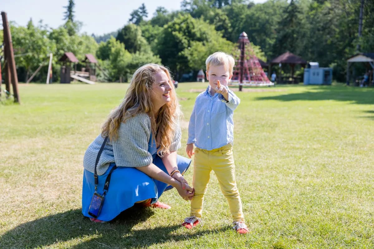 Coachin geht in die Hocke neben einem Kleinkind, das über eine sonnige Wiese läuft